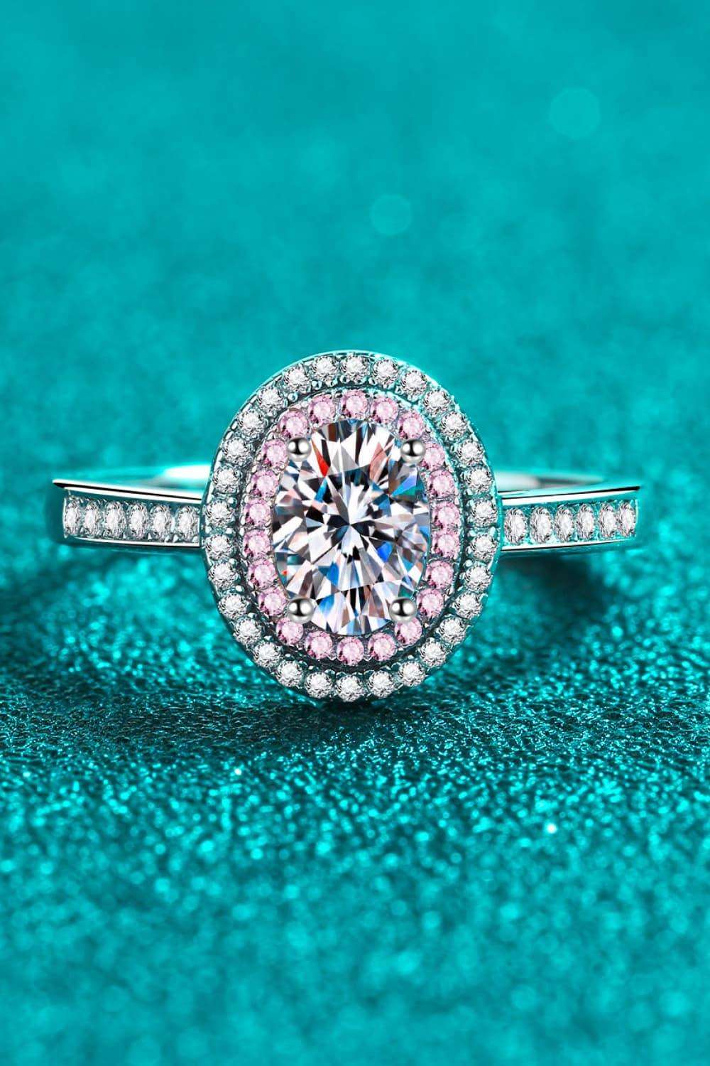 Sparkling oval-shaped diamond engagement ring with pave-set diamonds on a turquoise background.