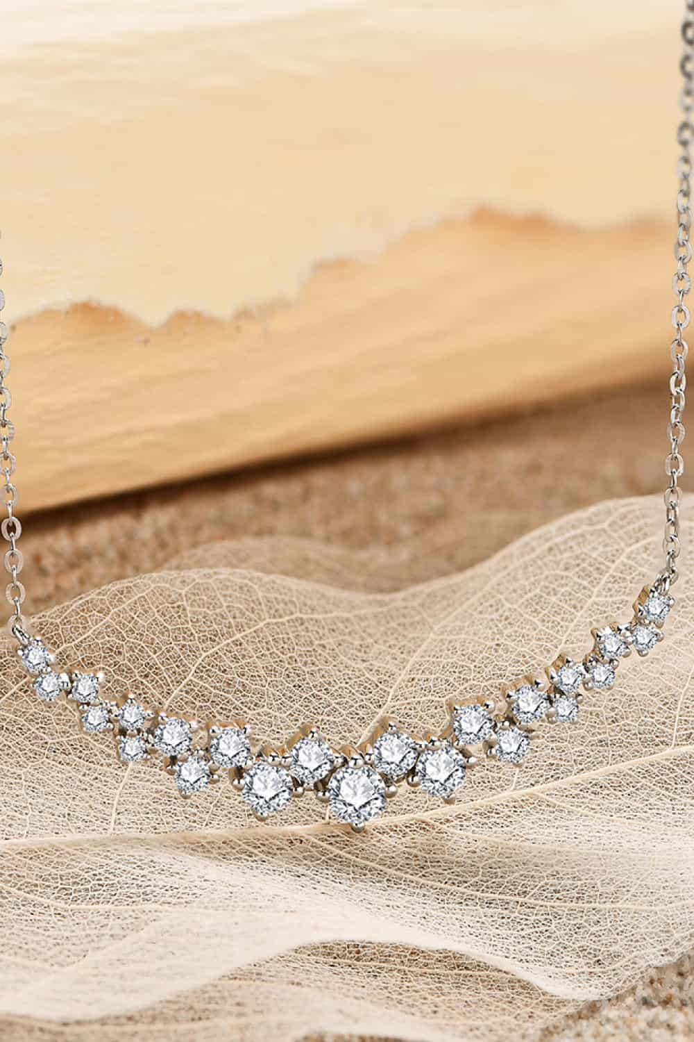 Elegant sterling silver necklace with 1.64 carat moissanite stones, displayed on sheer fabric against a beige desert backdrop.