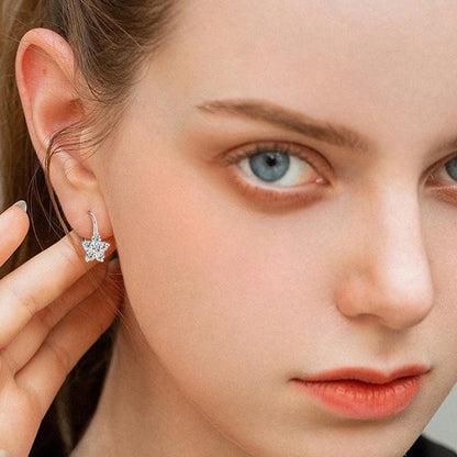 Elegant silver moissanite star-shaped huggie earrings adorning a model's face with striking blue eyes and natural makeup.