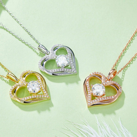 Elegant heart-shaped sterling silver and gold-tone moissanite pendants on delicate chains, surrounded by lush greenery.