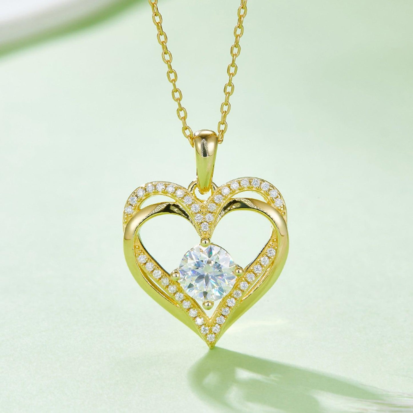 Elegant Heart-Shaped Moissanite Necklace in 925 Sterling Silver. The necklace features a sparkling heart-shaped pendant adorned with a central Moissanite gemstone and surrounded by delicate pavé-set crystals. Suspended from a fine gold-plated chain, this stylish pendant adds a touch of romance and sophistication.