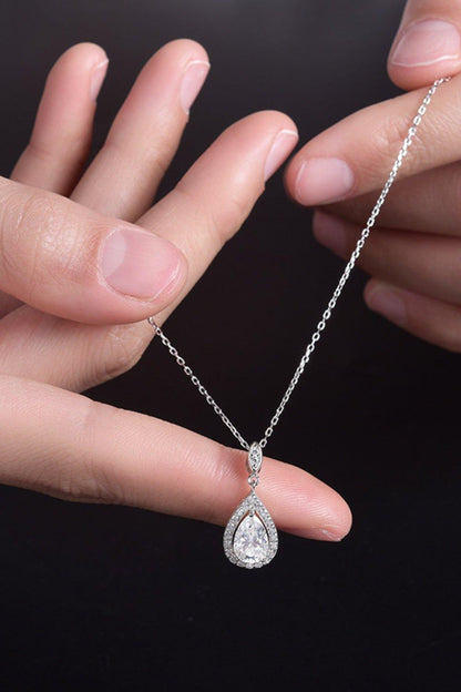 Elegant teardrop-shaped moissanite necklace on silver chain held in female hands against dark background