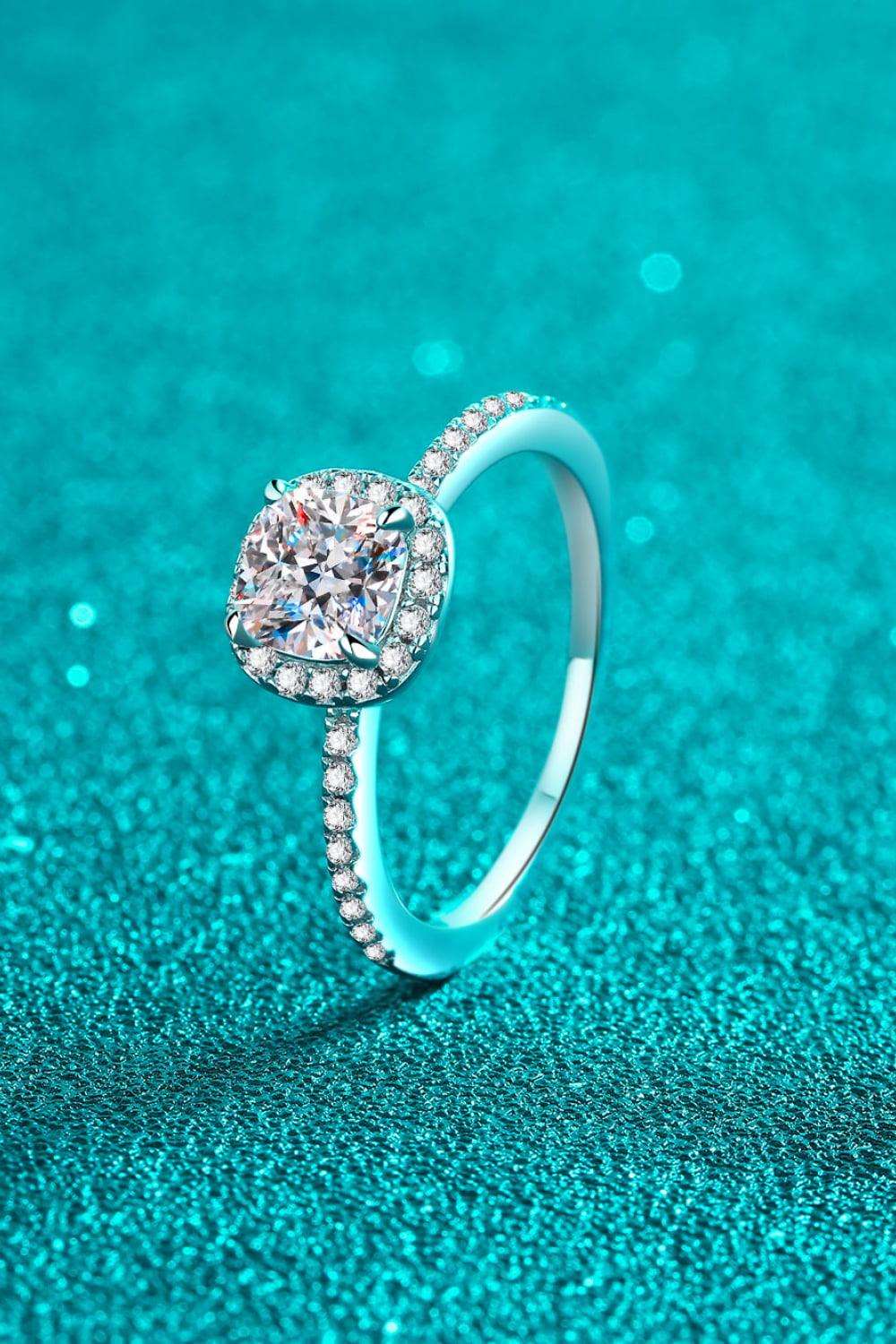 Elegant Moissanite Halo Ring - Sparkling diamond-like center stone surrounded by glittering sterling silver setting on teal background.