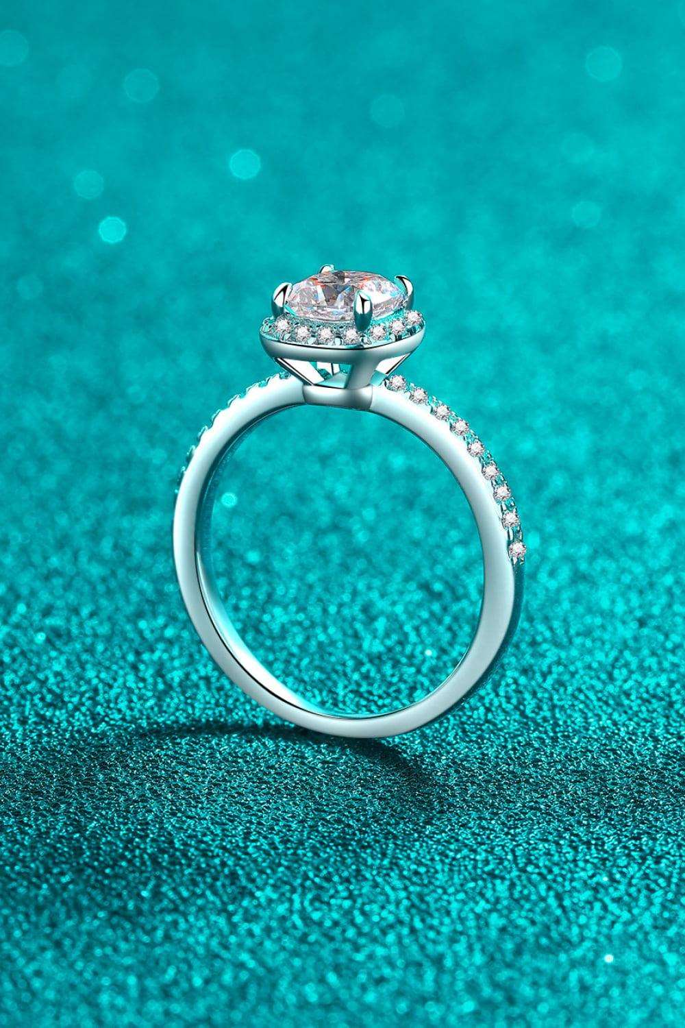 Elegant moissanite engagement ring with sparkling diamond halo on shimmering teal background