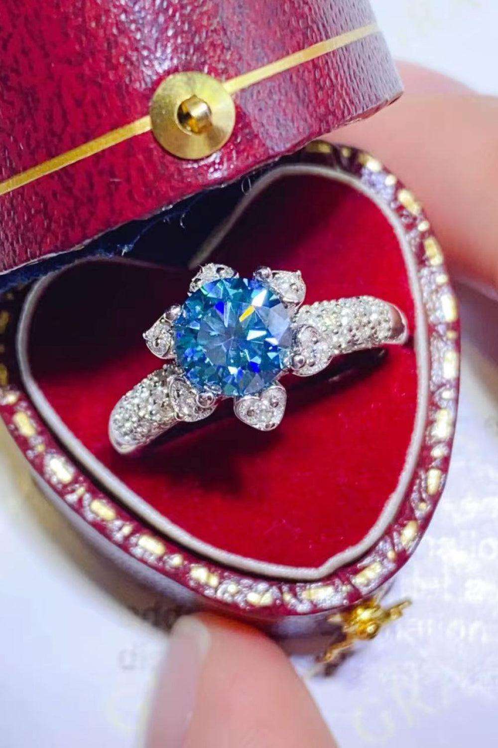 Sparkling moissanite flower ring in heart-shaped jewelry box, surrounded by vibrant red accents and golden details.