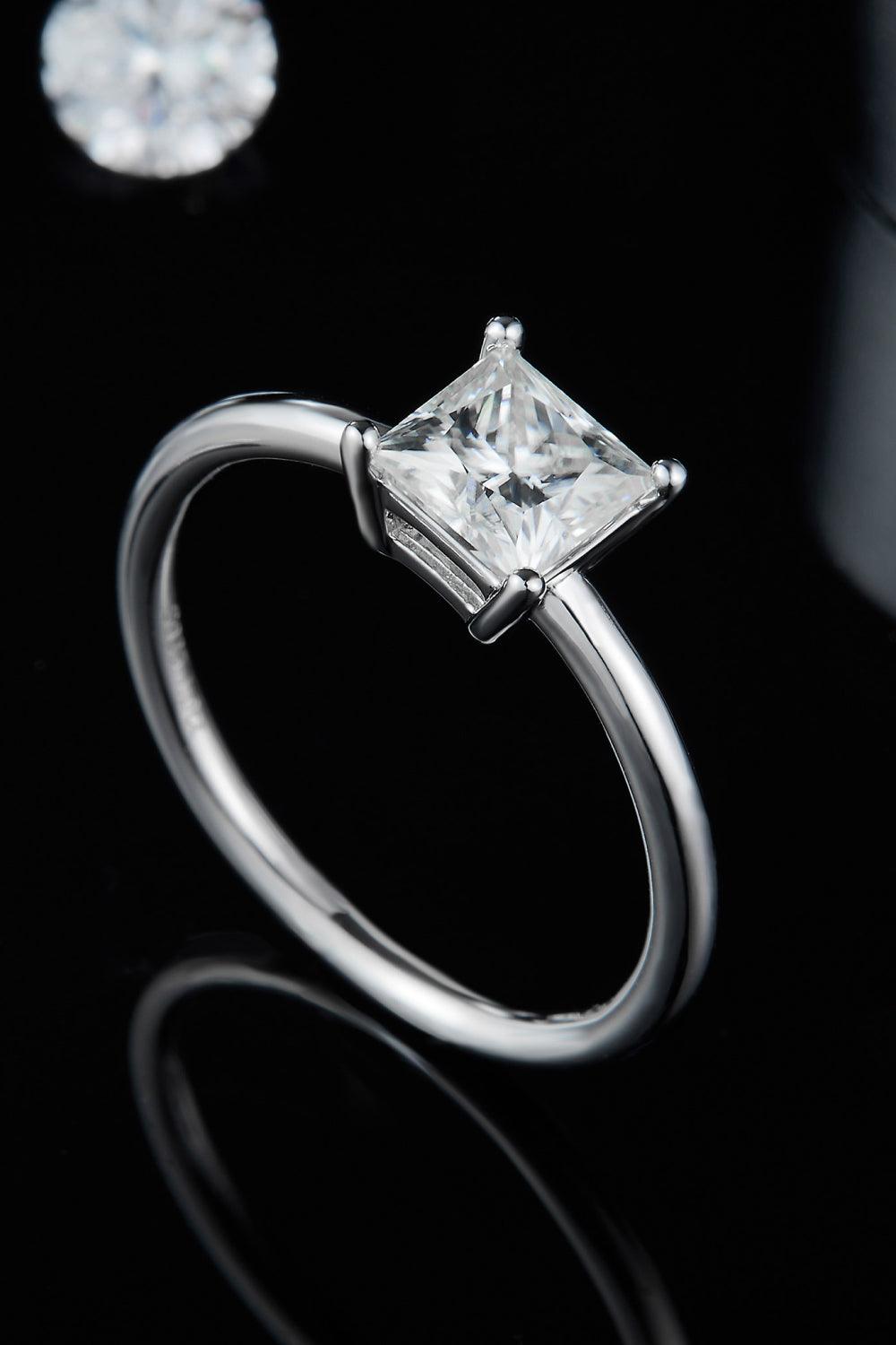 Elegant sterling silver solitaire ring with a sparkling princess-cut moissanite center stone, showcased against a dark backdrop.