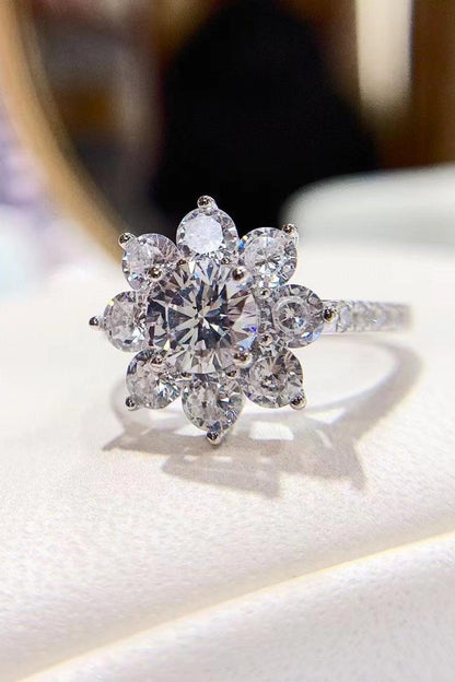 Elegant moissanite flower ring with dazzling round center stone surrounded by sparkling petal-shaped accents, set in a sleek silver-toned metal band.