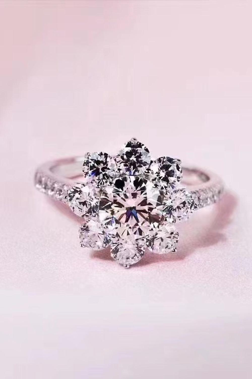 Elegant diamond flower-shaped engagement ring with sparkling gems on a soft pink background