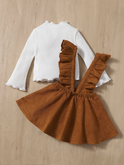 a little girl wearing a brown skirt and white top