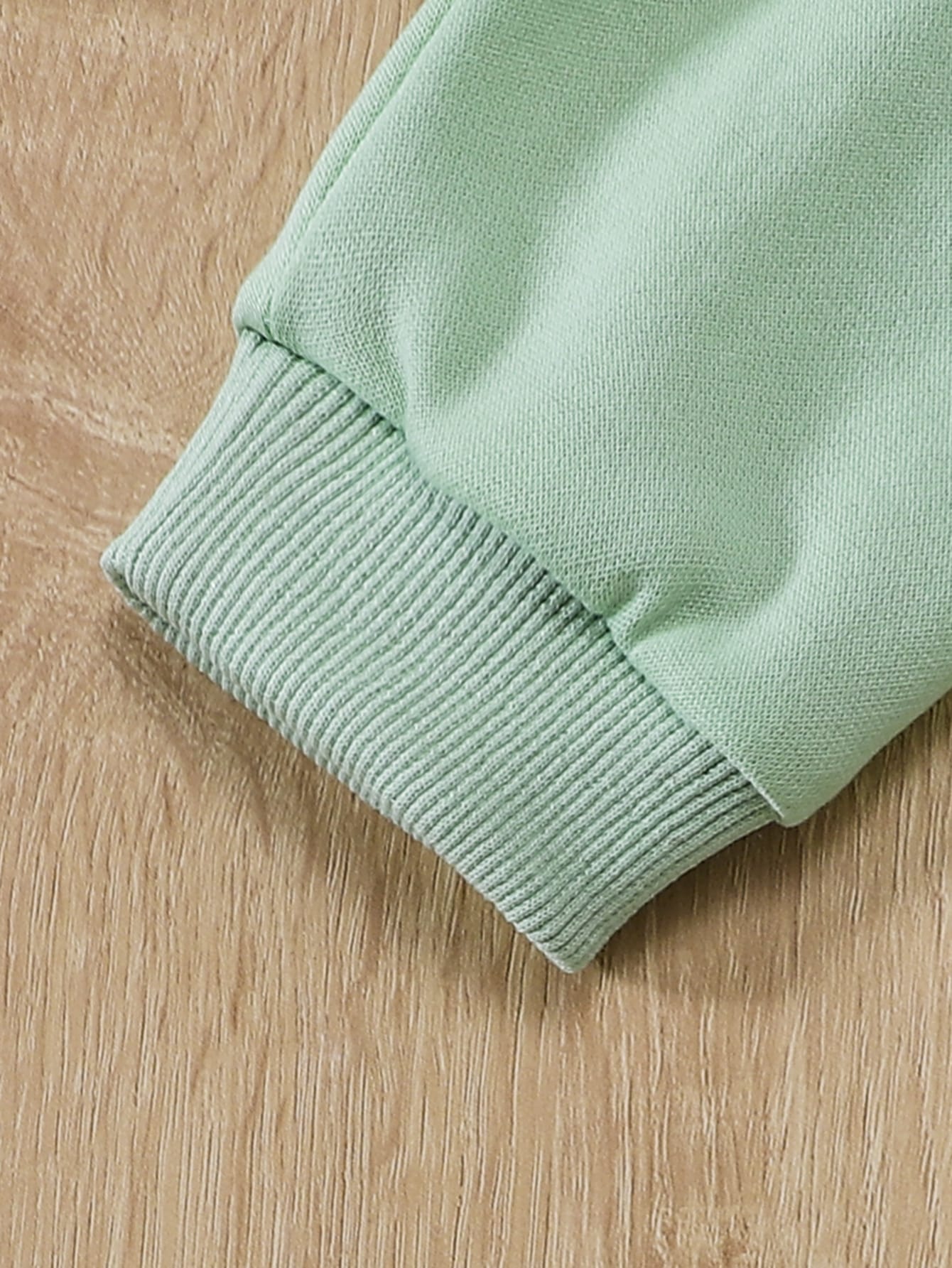 a green sweater laying on a wooden surface