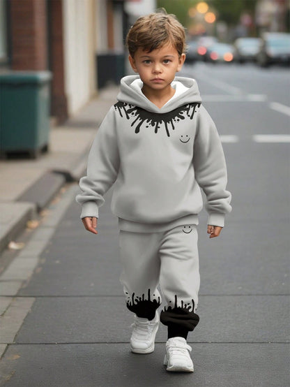 a little boy walking down the street wearing a grey sweatshirt and sweatpants