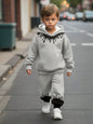 a little boy walking down the street wearing a grey sweatshirt and sweatpants