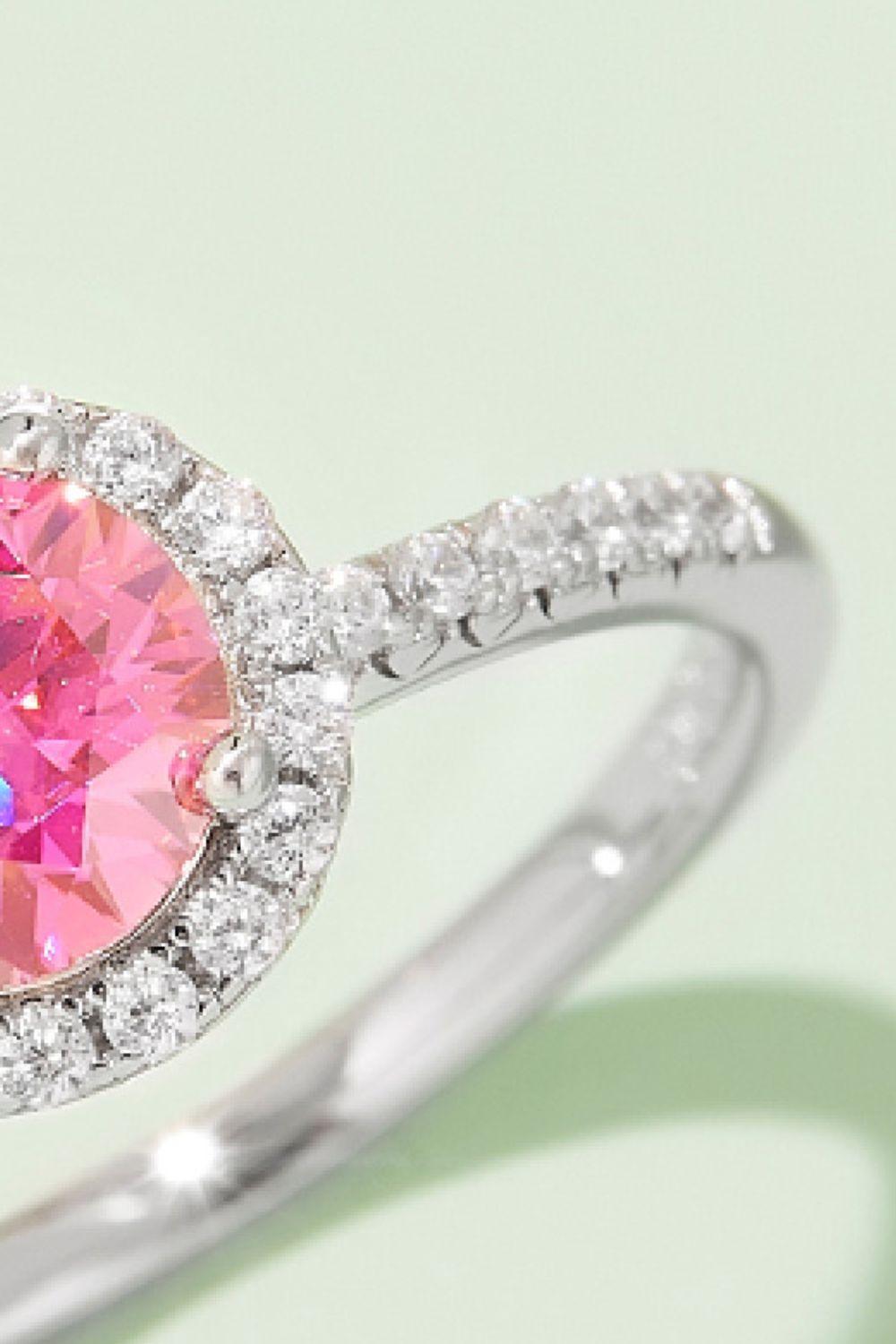 Elegant silver-toned ring with a vibrant pink center stone surrounded by a halo of sparkling white diamonds, set against a plain background.