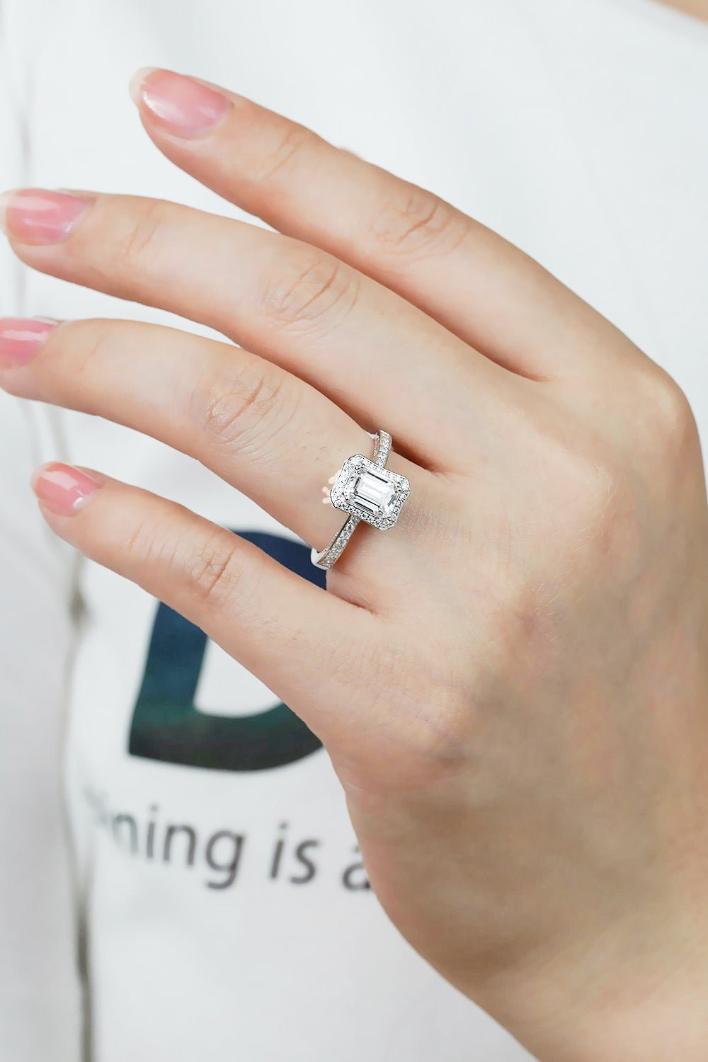 Elegant moissanite engagement ring on female hand against white background