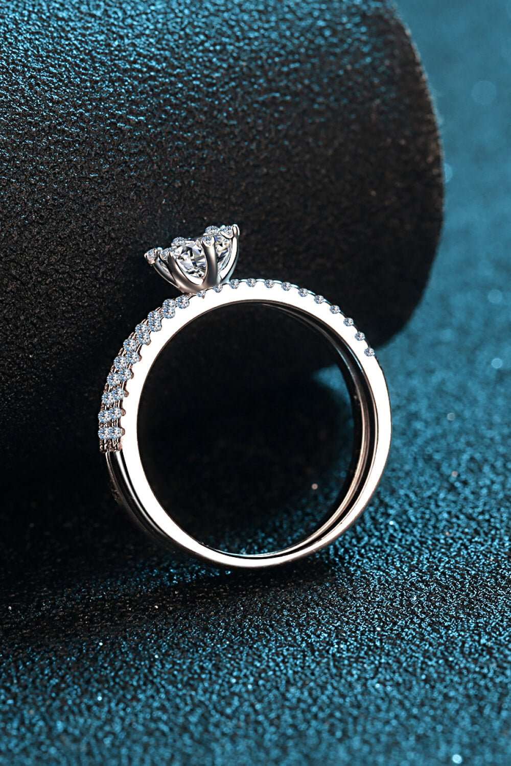 Elegant 1 Carat Moissanite Ring with Sparkling Diamond Accents on Textured Teal Surface