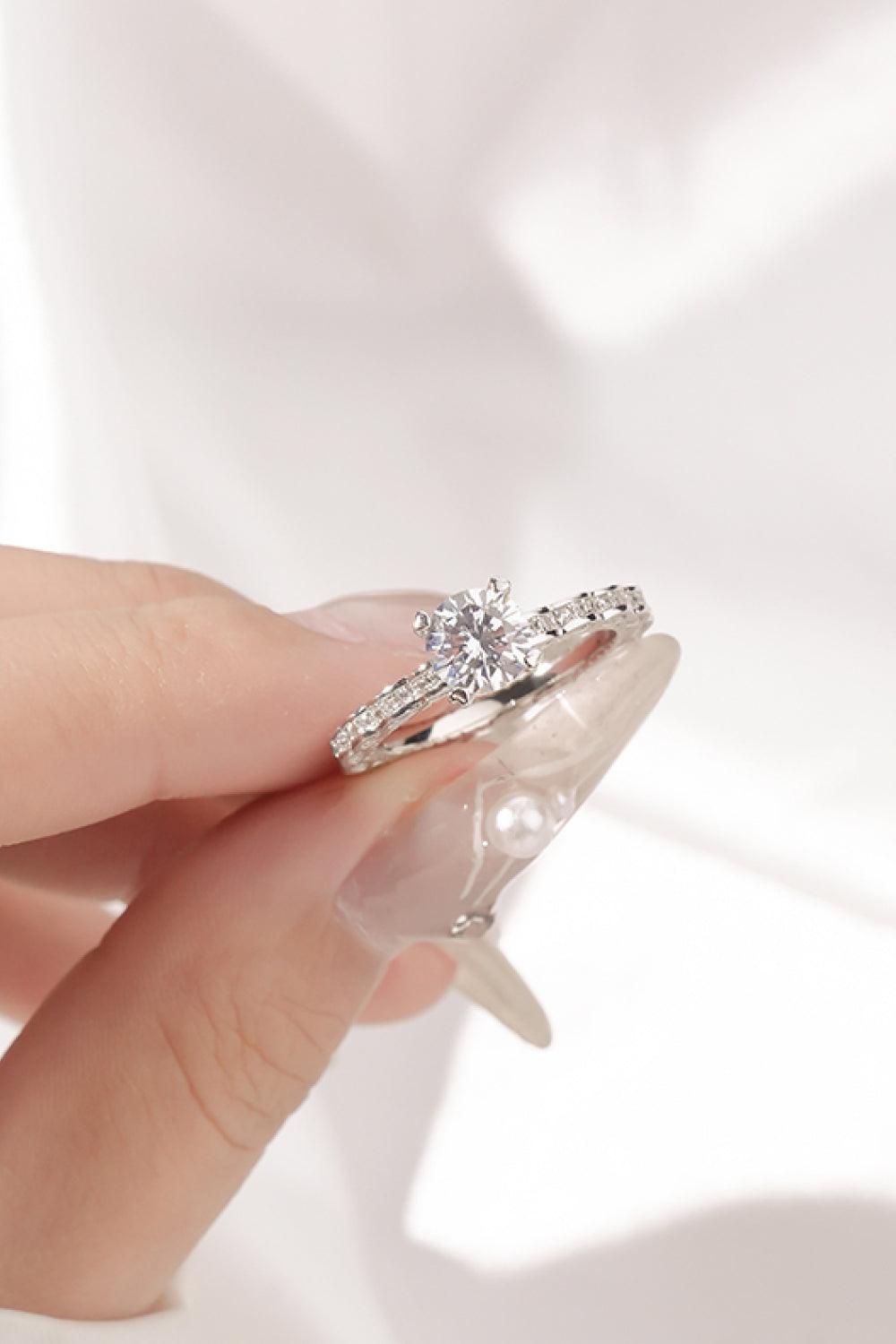 Elegant sterling silver ring with shimmering moissanite center stone and sparkling diamond accents, showcased on a woman's hand.