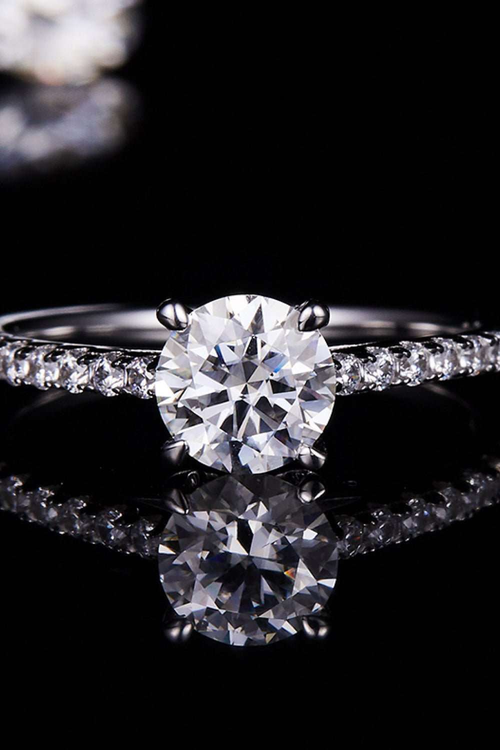 Elegant diamond engagement ring with a round brilliant-cut center stone and pavé-set side stones displayed against a reflective black background