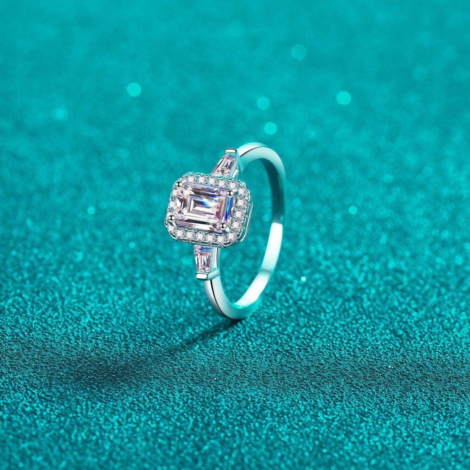 Elegant Moissanite Sterling Silver Ring - Captivating emerald-cut center stone surrounded by delicate accent stones, set against a mesmerizing turquoise background.