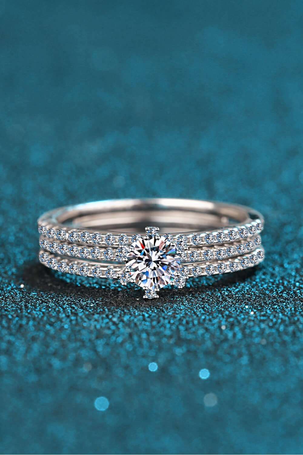 Elegant diamond rings on teal background. Sparkling solitaire engagement ring with pave set diamond band. Luxury jewelry display with glamorous ring.