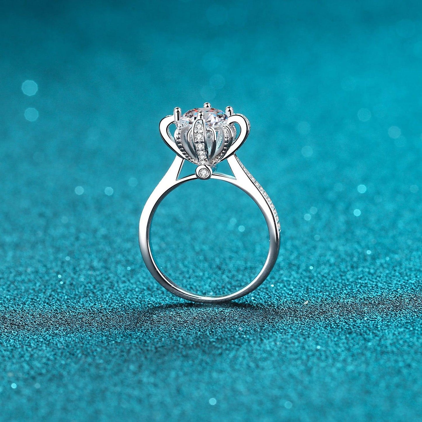 Elegant sterling silver moissanite ring with a captivating crown design, set against a shimmering teal background.