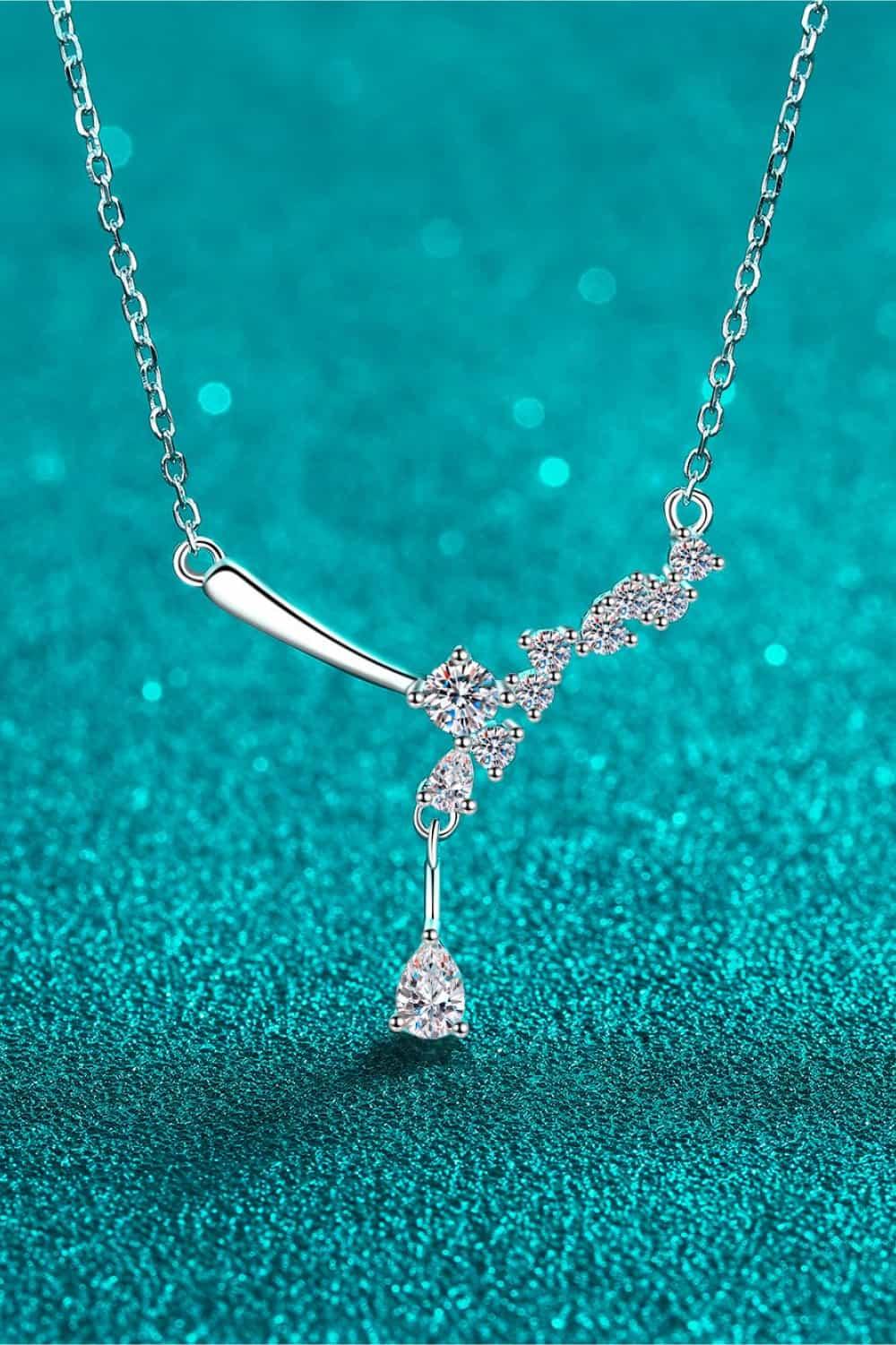 Delicate silver necklace with a pendant featuring a cluster of sparkling diamonds against a vibrant teal background.