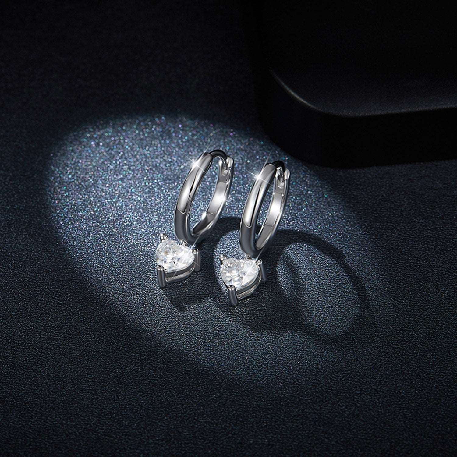 Elegant silver hoop earrings with sparkling cubic zirconia accents placed on a dark textured surface.