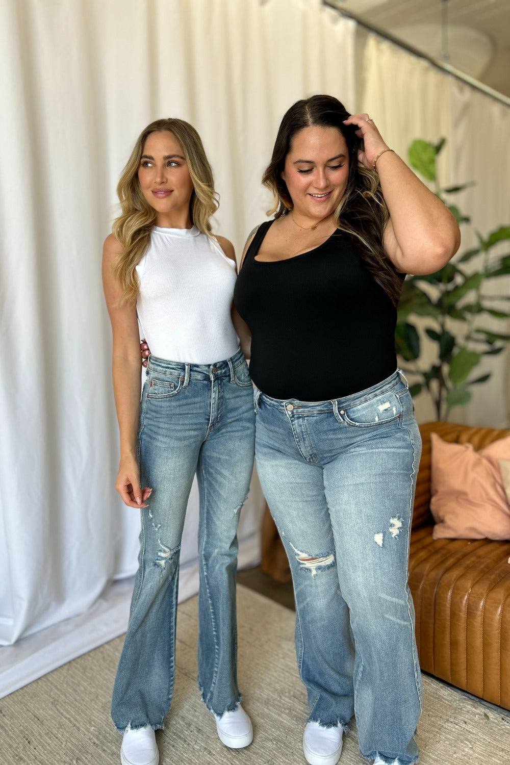 two women standing next to each other in jeans