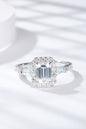 Elegant moissanite and diamond ring, featuring an emerald-cut center stone surrounded by a halo of sparkling accent stones, set in sleek sterling silver.