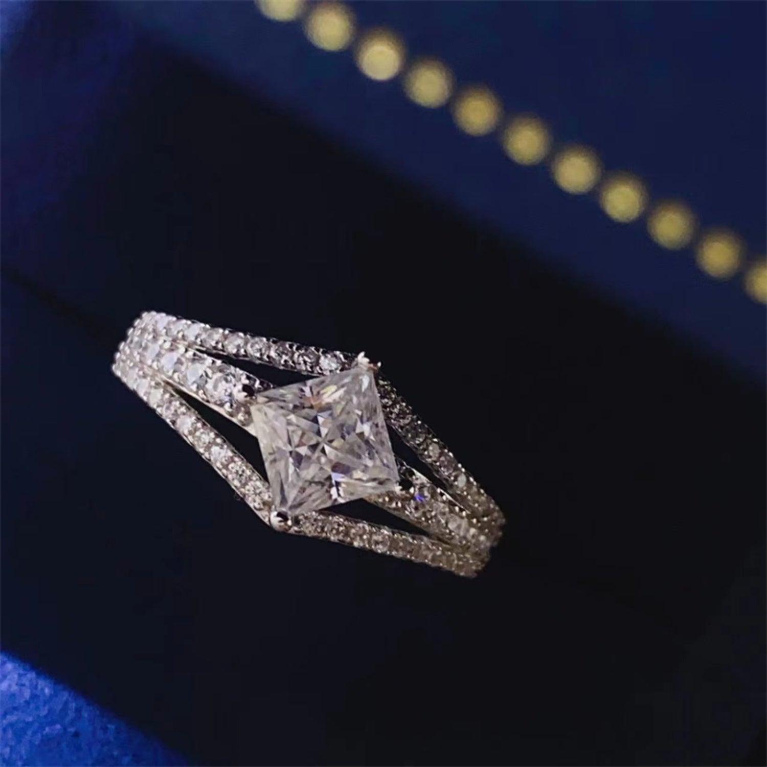 Elegant princess-cut diamond ring with pave-set diamond accents on a dark blue background.