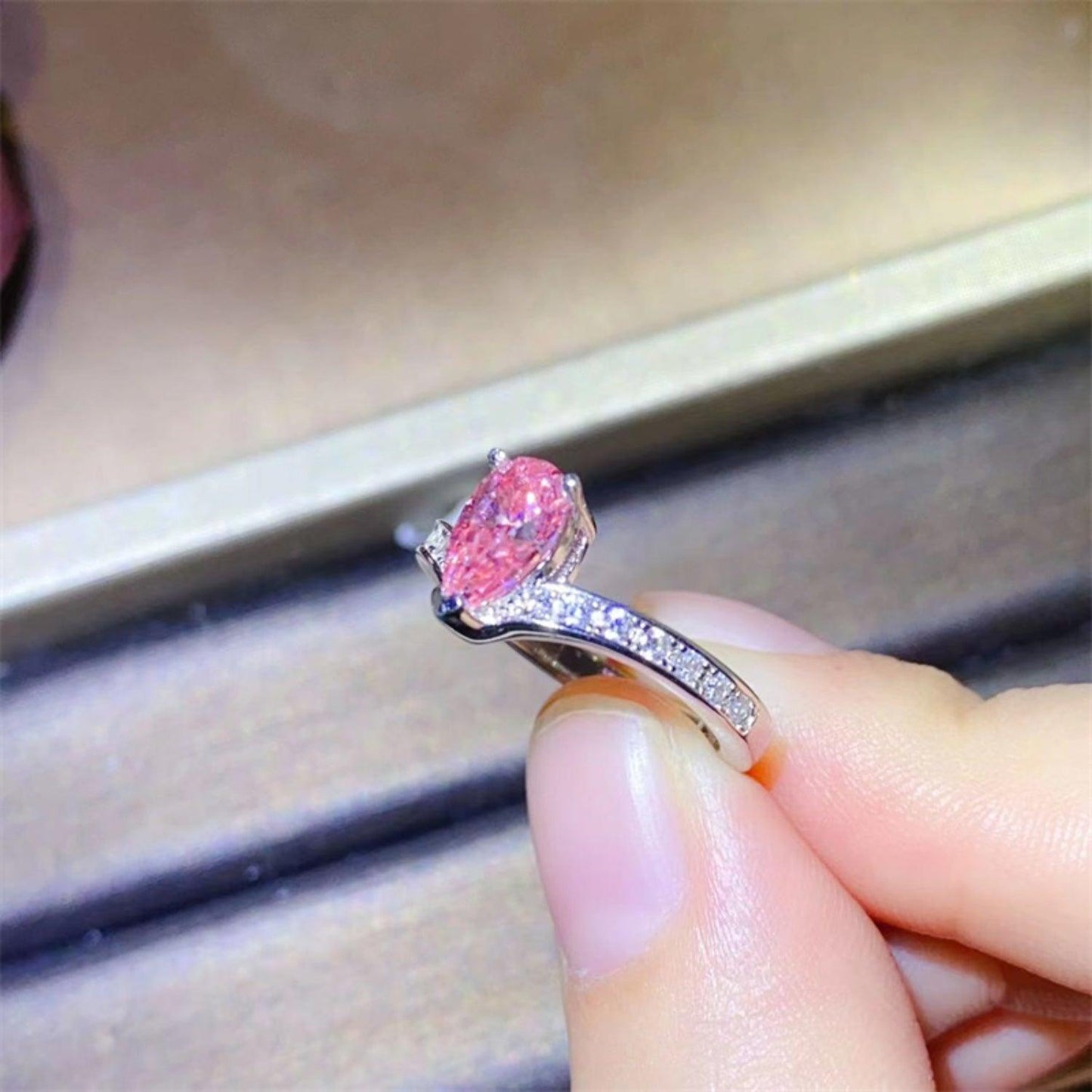 Elegant pink moissanite gemstone ring on a woman's hand. The stunning, oval-shaped moissanite is set in a sleek sterling silver band with delicate pave diamond accents, creating a stunning and sophisticated piece of jewelry.