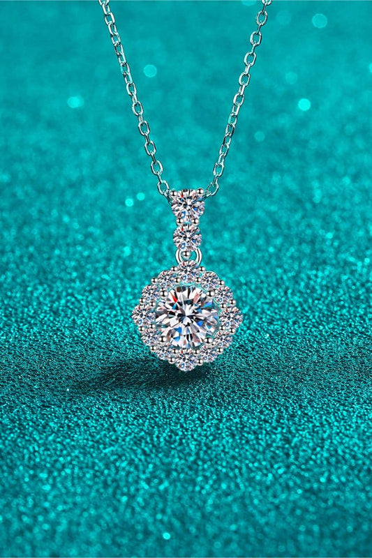 Elegant Moissanite Pendant Necklace: Sparkling 1 carat moissanite stone set in a sterling silver halo design, displayed on a delicate silver chain against a captivating turquoise backdrop.