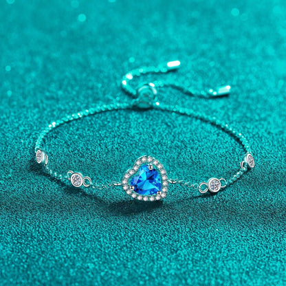 Elegant heart-shaped blue gemstone bracelet with sparkling accents, resting on a vibrant teal background.