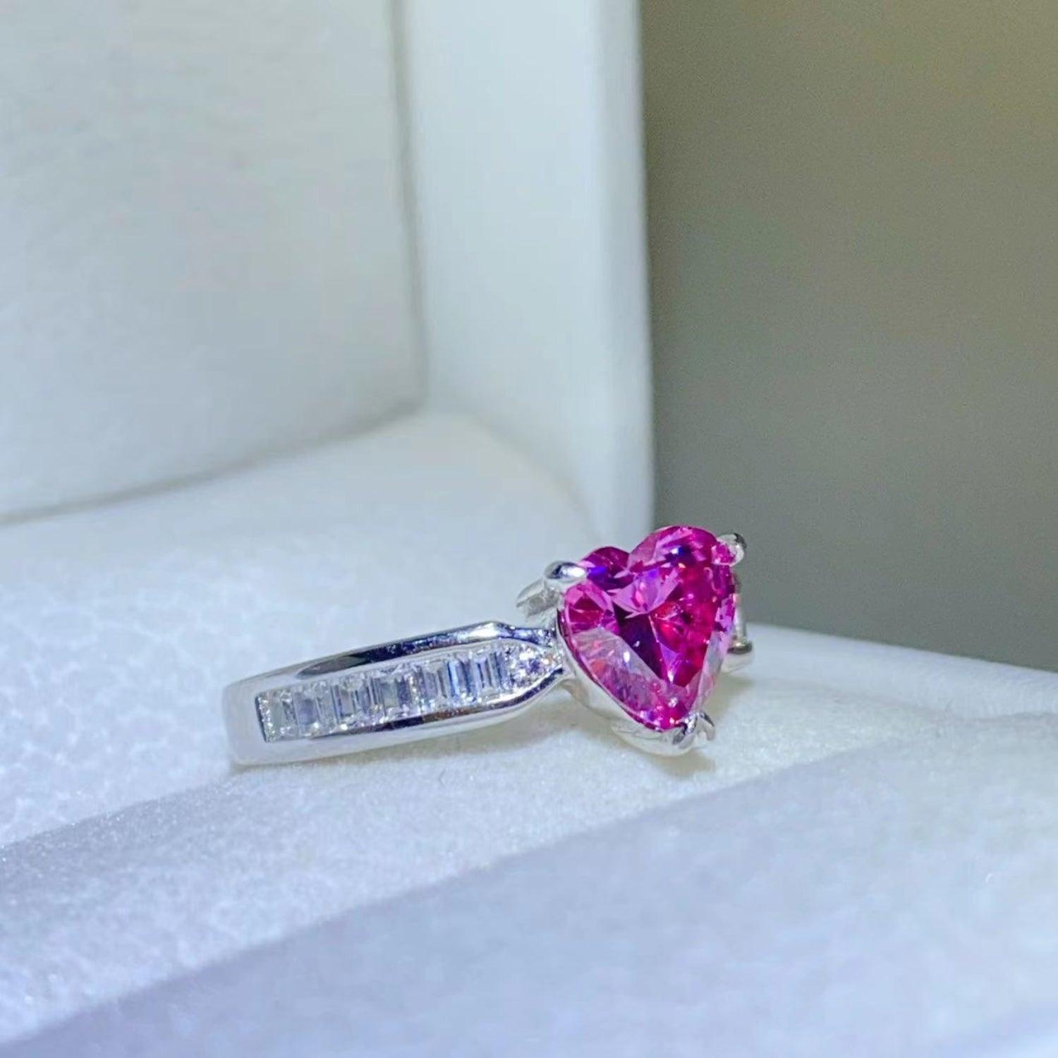 Elegant pink heart-shaped moissanite stone ring with baguette accent stones on a white display surface