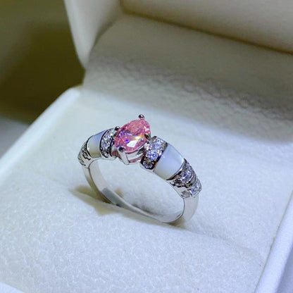 Elegant sterling silver ring with large oval-shaped pink moissanite stone and smaller accent stones, displayed on white cushioned surface.