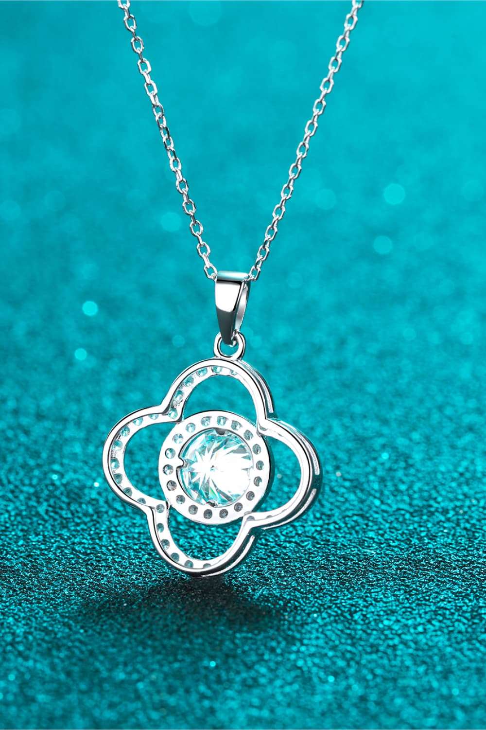 Elegant silver necklace with a sparkling cubic zirconia pendant in the shape of a flower, placed on a teal glittery background.