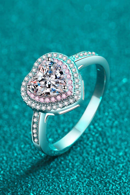 Elegant heart-shaped moissanite engagement ring with sparkling diamond accents set in sterling silver against a teal background.