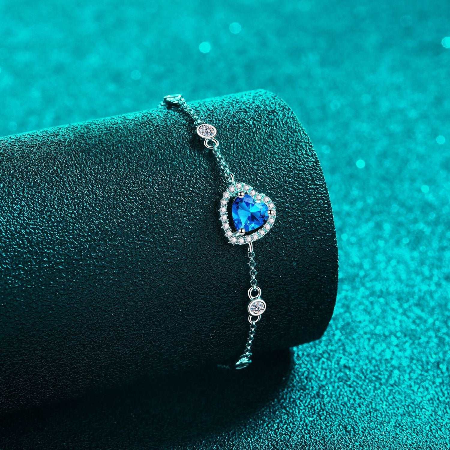 1 Carat Moissanite 925 Sterling Silver Heart-Shaped Bracelet on a black textured background with a teal blue, blurred background.