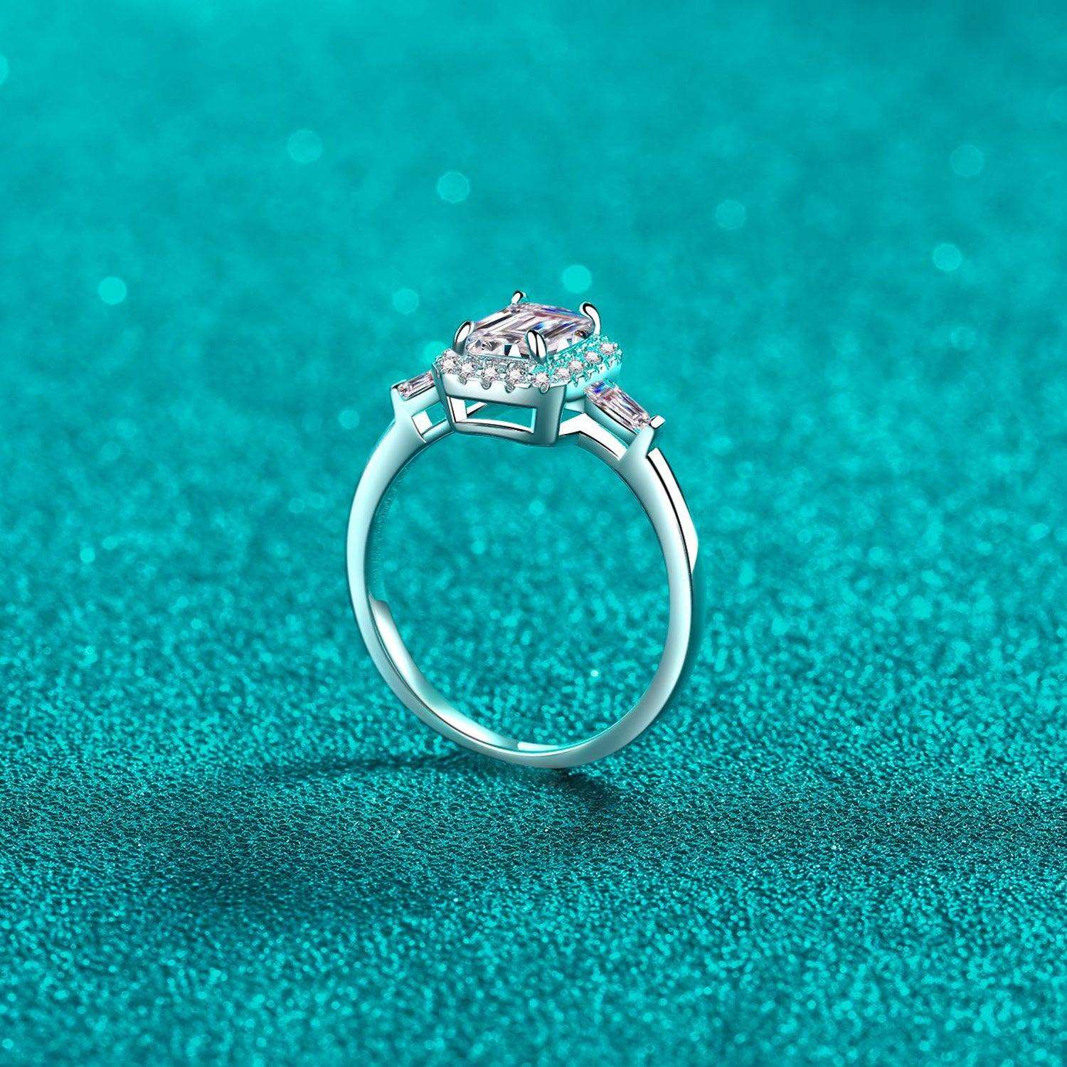 Elegant sterling silver ring with sparkling 1 carat moissanite stone, set against a vibrant turquoise background.