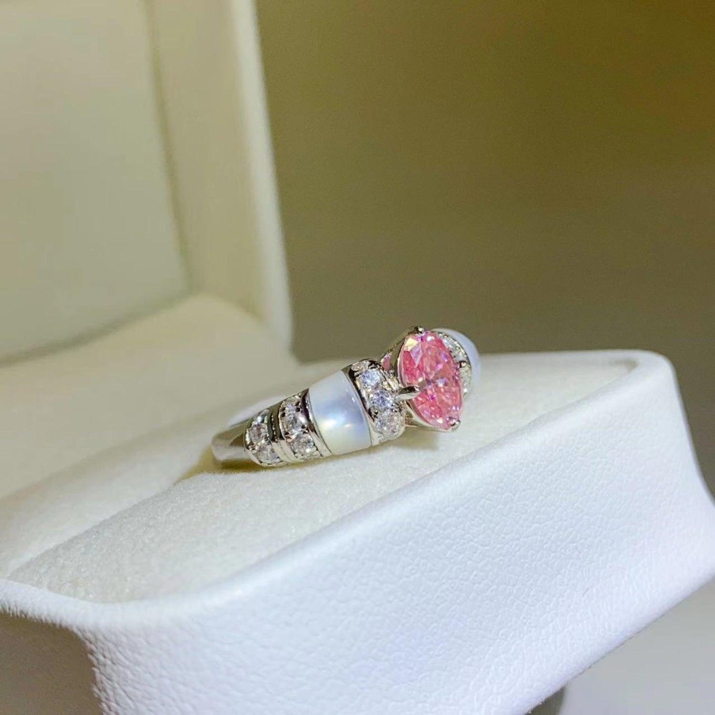 Elegant sterling silver ring with a sparkling pink moissanite center stone and diamond accents, displayed on a white jewelry box.