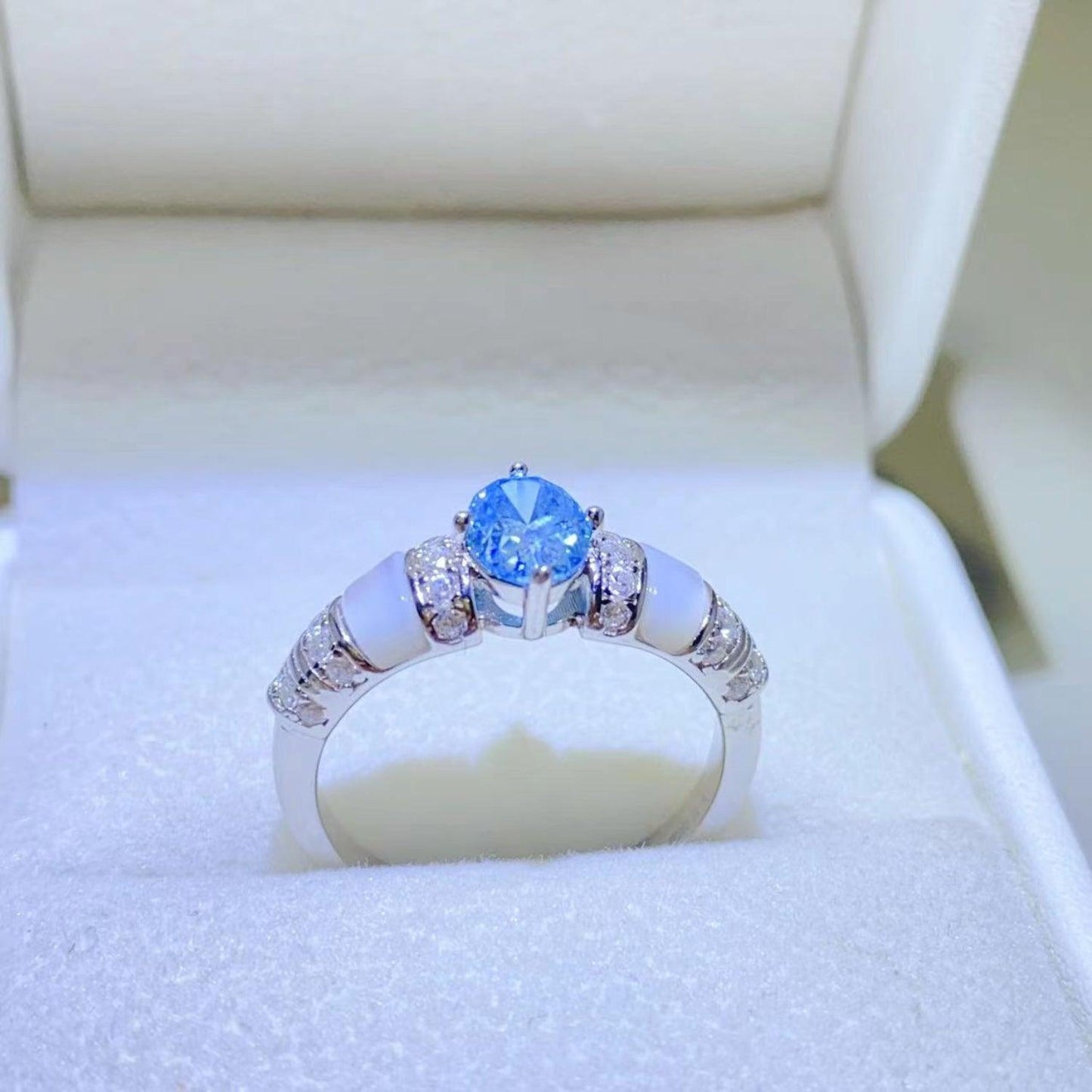 Elegant sterling silver ring with a sparkling 1 carat moissanite center stone and decorative side stones, displayed on a white cushion in a jewelry box.